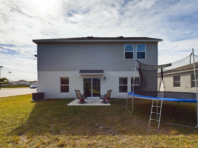 rear view of house featuring a yard, central AC unit, a patio area, and a trampoline