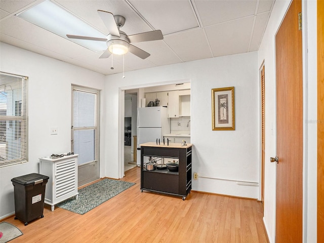 kitchen with white cabinets, backsplash, white refrigerator, ceiling fan, and light hardwood / wood-style flooring