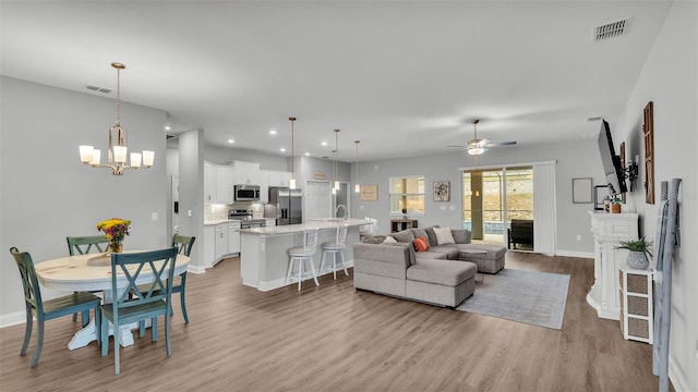 living room with ceiling fan with notable chandelier, sink, and light wood-type flooring