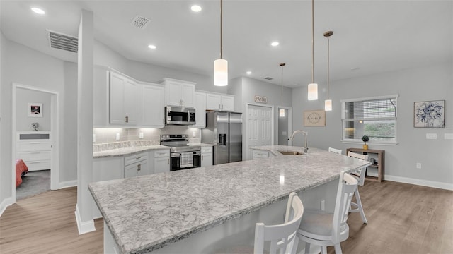 kitchen with sink, white cabinetry, hanging light fixtures, a large island with sink, and appliances with stainless steel finishes