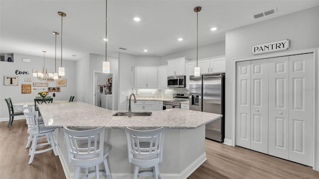 kitchen featuring sink, a breakfast bar, hanging light fixtures, stainless steel appliances, and white cabinets