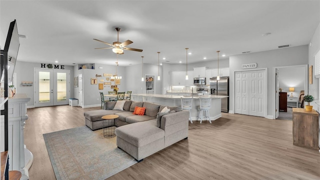 living room featuring french doors, ceiling fan, and light wood-type flooring