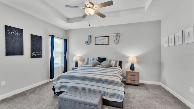 carpeted bedroom featuring ceiling fan and a tray ceiling