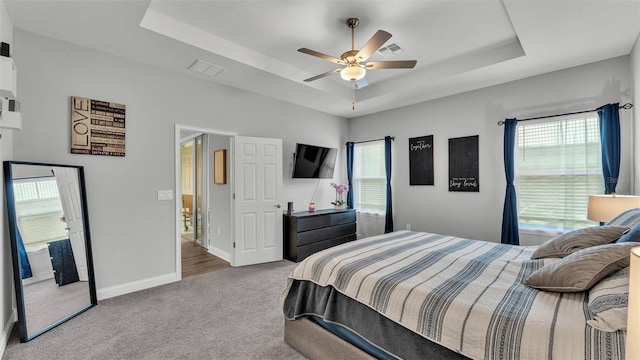 carpeted bedroom with ceiling fan, a tray ceiling, and multiple windows