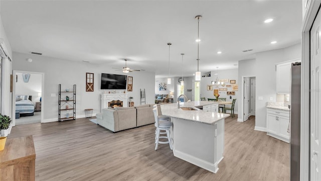 kitchen featuring sink, white cabinets, hanging light fixtures, a kitchen island with sink, and light stone countertops