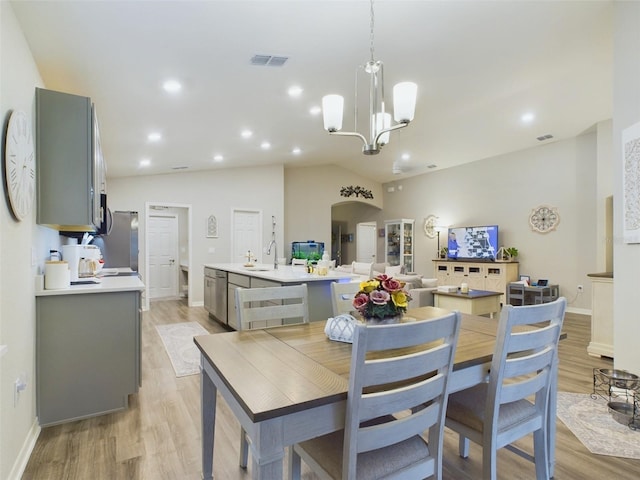 dining room featuring an inviting chandelier, lofted ceiling, sink, and light hardwood / wood-style flooring