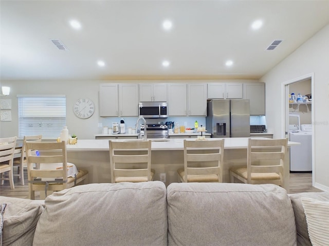 kitchen featuring a breakfast bar, separate washer and dryer, light hardwood / wood-style flooring, an island with sink, and stainless steel appliances