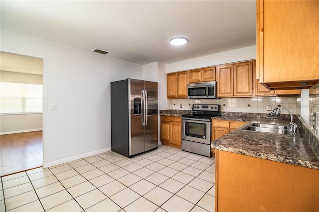 kitchen featuring sink, light tile patterned floors, stainless steel appliances, tasteful backsplash, and dark stone counters