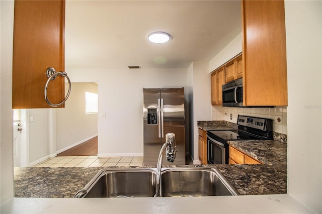 kitchen with tasteful backsplash, appliances with stainless steel finishes, sink, and dark stone countertops