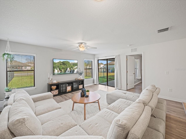 living room featuring ceiling fan, a healthy amount of sunlight, a textured ceiling, and light hardwood / wood-style floors