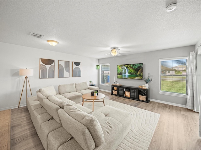 living room featuring ceiling fan, a textured ceiling, and light wood-type flooring