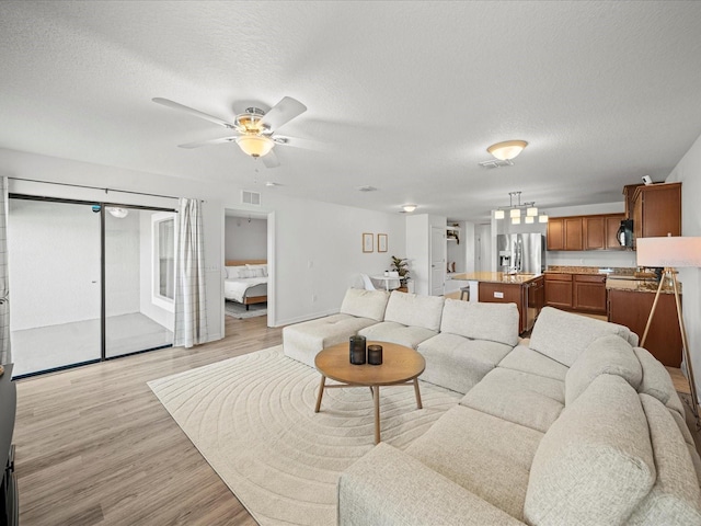 living room with ceiling fan, a textured ceiling, and light wood-type flooring