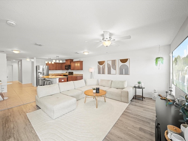 living room with ceiling fan, light hardwood / wood-style floors, and a textured ceiling