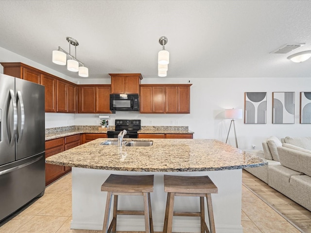 kitchen featuring light tile patterned flooring, decorative light fixtures, sink, black appliances, and a center island with sink