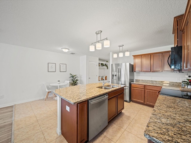 kitchen featuring sink, appliances with stainless steel finishes, pendant lighting, light stone countertops, and a kitchen island with sink