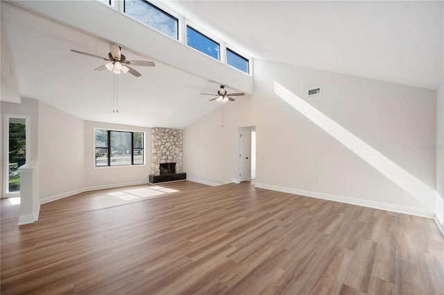 unfurnished living room with ceiling fan, a stone fireplace, vaulted ceiling, and light wood-type flooring