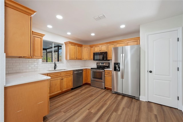 kitchen featuring stainless steel appliances, sink, light hardwood / wood-style floors, and decorative backsplash