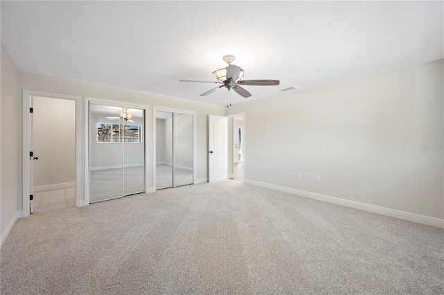 unfurnished bedroom with two closets, light colored carpet, and ceiling fan