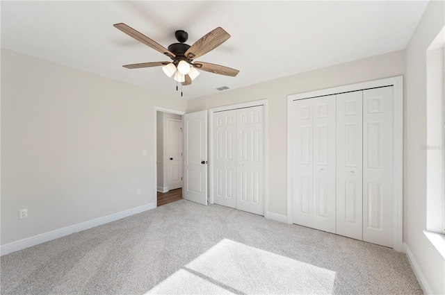 unfurnished bedroom with multiple closets, ceiling fan, and light carpet