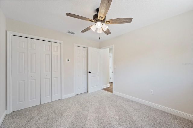 unfurnished bedroom with multiple closets, ceiling fan, and light colored carpet