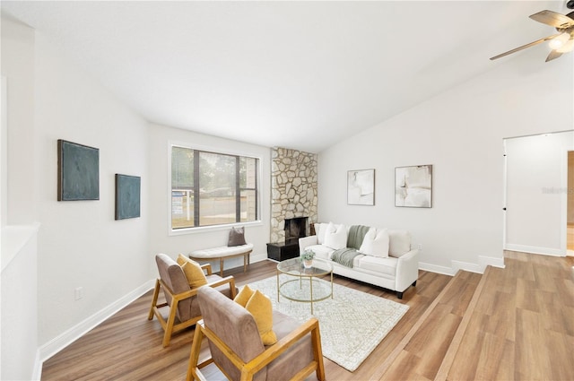 living room with lofted ceiling, a stone fireplace, light wood finished floors, and ceiling fan