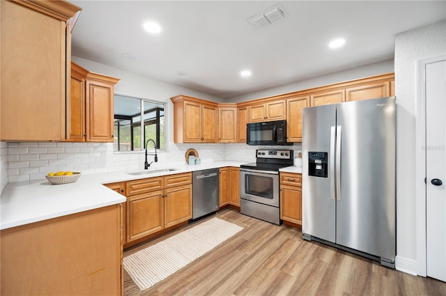 kitchen with stainless steel appliances, a sink, light wood-style flooring, tasteful backsplash, and light countertops