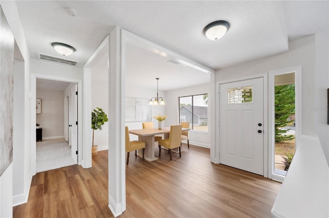 foyer with light wood-style flooring, baseboards, a chandelier, and a textured ceiling