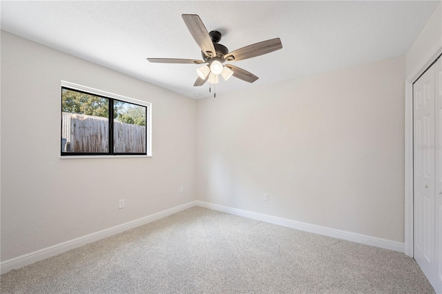 carpeted spare room featuring ceiling fan and baseboards
