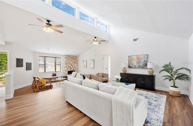 living area with a stone fireplace, high vaulted ceiling, ceiling fan, light wood-style flooring, and baseboards