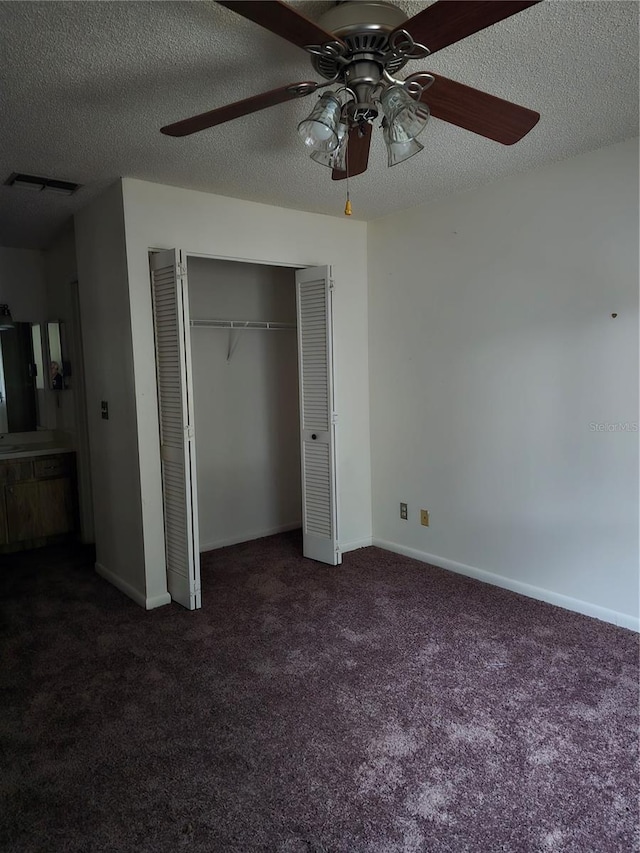 unfurnished bedroom featuring a closet, ceiling fan, dark carpet, and a textured ceiling