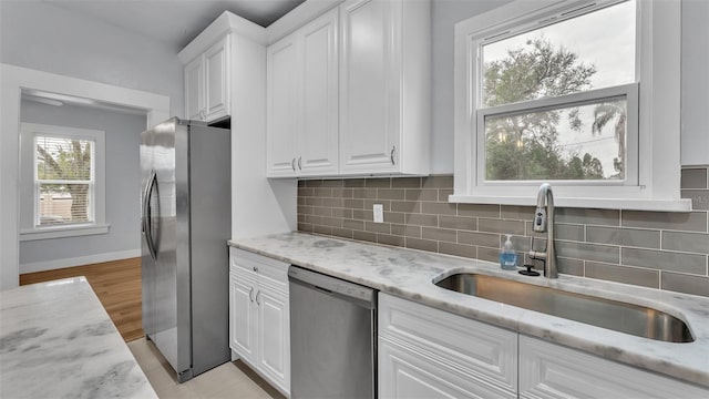 kitchen featuring stainless steel appliances, light stone countertops, sink, and white cabinets