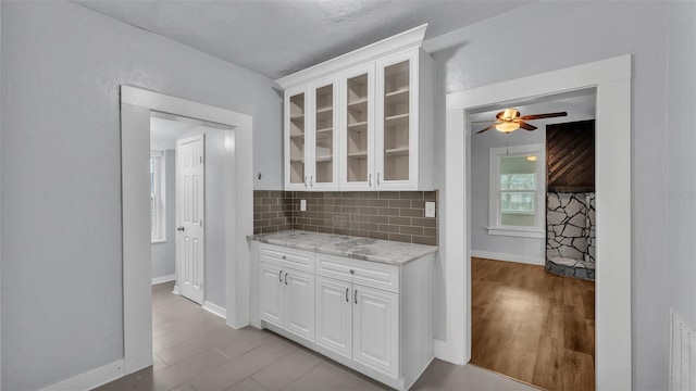 kitchen featuring light hardwood / wood-style flooring, ceiling fan, backsplash, light stone counters, and white cabinets