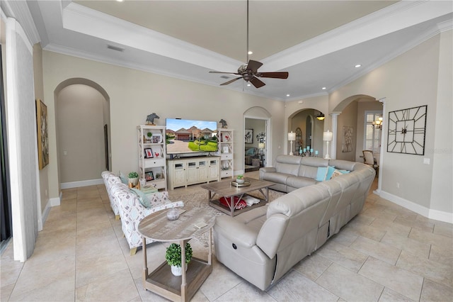 living room featuring decorative columns, light tile patterned floors, ceiling fan, a tray ceiling, and crown molding