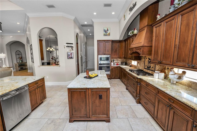 kitchen featuring premium range hood, appliances with stainless steel finishes, tasteful backsplash, light stone countertops, and a kitchen island