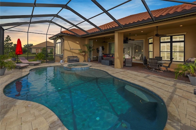 pool at dusk featuring an in ground hot tub, ceiling fan, a patio area, and glass enclosure