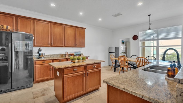 kitchen featuring sink, light stone countertops, an island with sink, black fridge, and decorative light fixtures