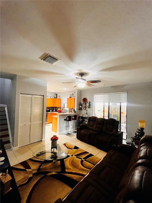 living room featuring ceiling fan, a textured ceiling, and light tile patterned floors