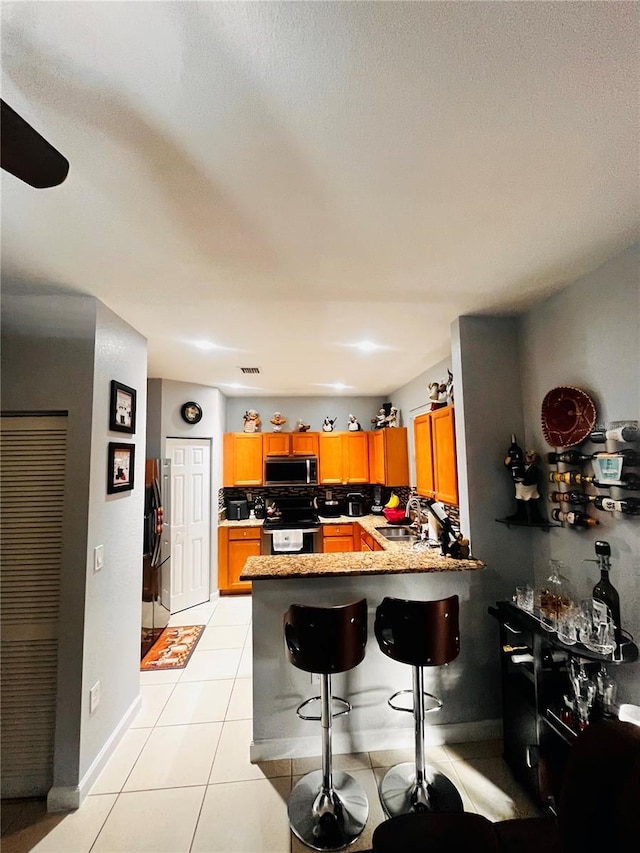 kitchen featuring a breakfast bar area, tasteful backsplash, light tile patterned floors, stainless steel range, and kitchen peninsula