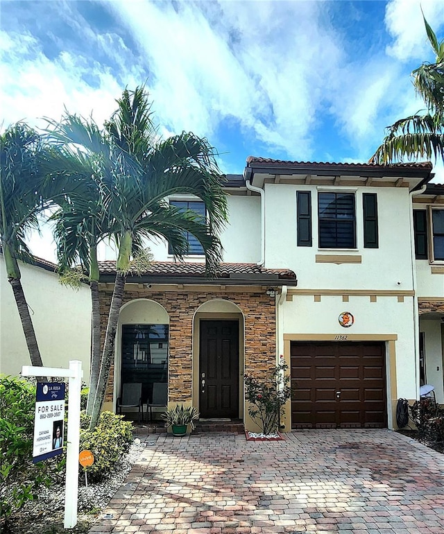 view of front facade featuring an attached garage, stone siding, a tiled roof, decorative driveway, and stucco siding