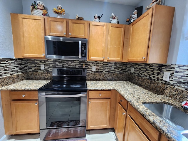 kitchen featuring light stone counters, light tile patterned floors, decorative backsplash, appliances with stainless steel finishes, and a sink