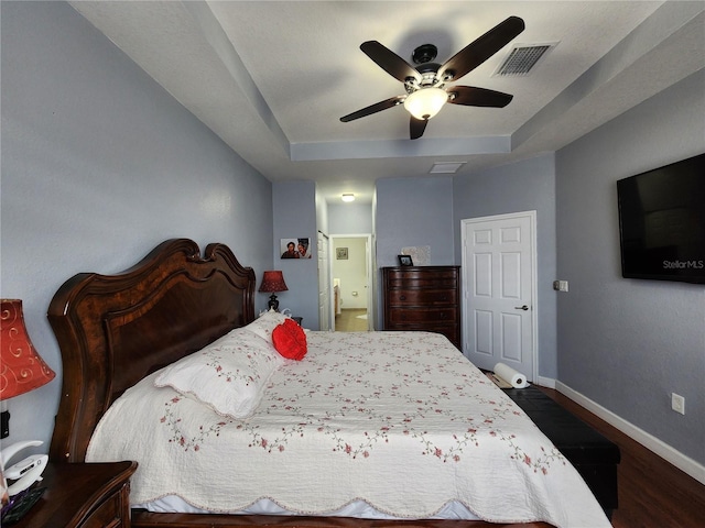 bedroom with baseboards, visible vents, a raised ceiling, connected bathroom, and dark wood-style floors