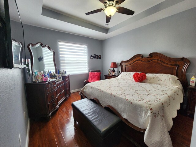 bedroom with dark wood-style floors, a raised ceiling, a ceiling fan, and baseboards