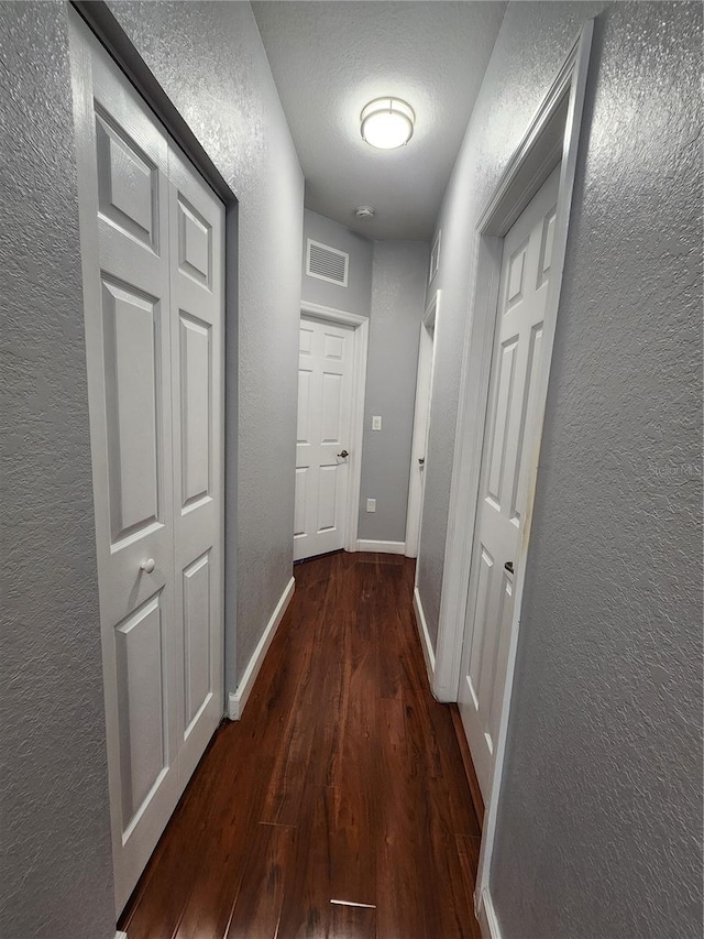 hallway with baseboards, visible vents, dark wood finished floors, and a textured wall