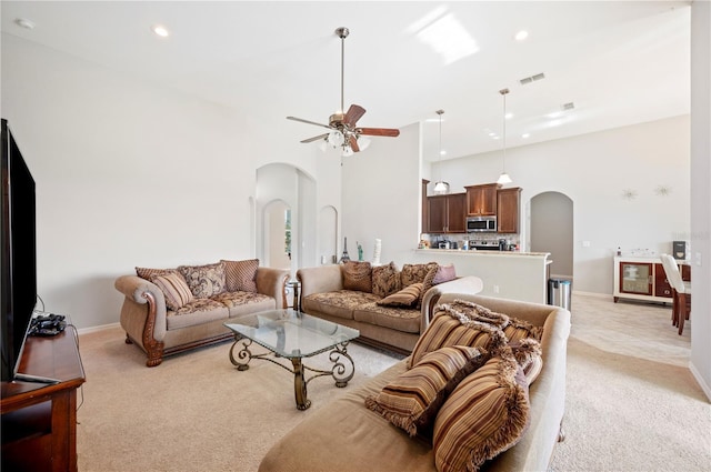 living area featuring arched walkways, light carpet, visible vents, and a ceiling fan