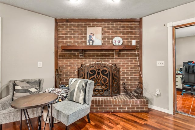 sitting room featuring wood-type flooring, a brick fireplace, and a textured ceiling