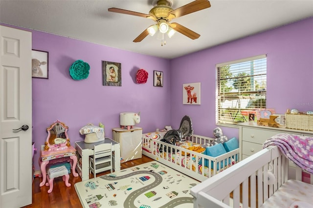 bedroom featuring dark hardwood / wood-style flooring, a nursery area, and ceiling fan