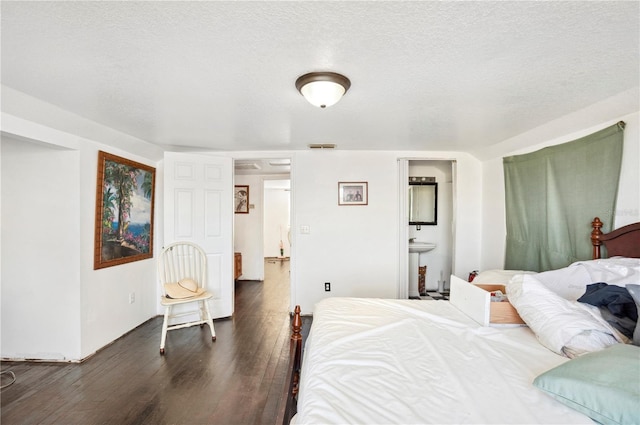 bedroom with dark wood-type flooring, ensuite bathroom, and a textured ceiling