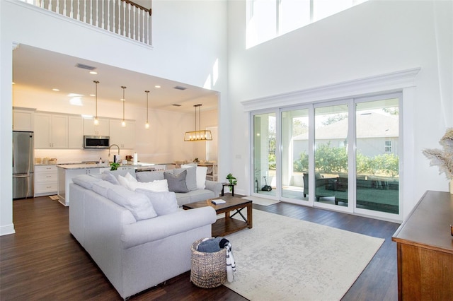 living room featuring dark wood-type flooring, an inviting chandelier, sink, and a high ceiling