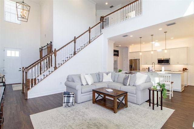 living room with sink, crown molding, an inviting chandelier, dark hardwood / wood-style flooring, and a high ceiling