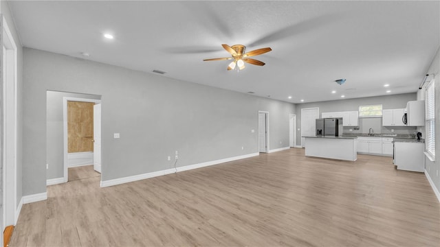 unfurnished living room with ceiling fan, sink, and light hardwood / wood-style flooring